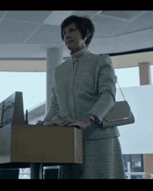 a woman in a suit stands at a podium holding a box