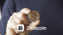 a person holding a coin in front of a 21bitcoin sign