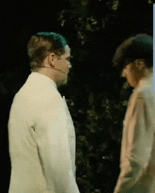 two men standing next to each other in a dark room with trees in the background