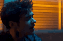 a man with curly hair is singing into a microphone in a dark room with a yellow light behind him .