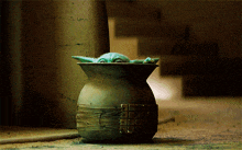 a statue of a frog is sitting in a green vase on the ground