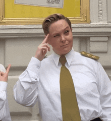 a woman wearing a white shirt and a gold tie holds her hand to her forehead