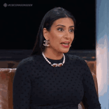 a woman wearing a pearl necklace and chanel earrings is sitting in a chair