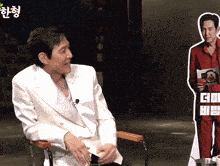 a man in a white jacket sits in front of a cardboard cutout of another man