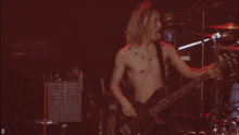 a shirtless man is playing a bass guitar on a stage
