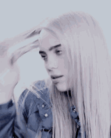 billie eilish is wearing a blue jacket and holding her hair in a close up of her face .