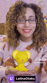 a woman with curly hair and glasses is holding a stuffed animal with wings and the hashtag latinaotaku at the bottom