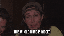 a man with long hair and a hat is saying this whole thing is rigged