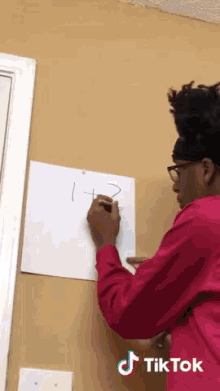 a man in a pink shirt is writing on a white board with tiktok written on the bottom right