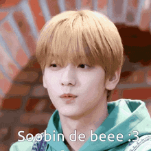 a young man with blonde hair is wearing a green hoodie and says soobin de bee