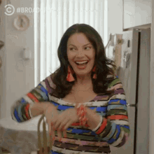 a woman in a colorful striped shirt is laughing in a kitchen with a refrigerator in the background .