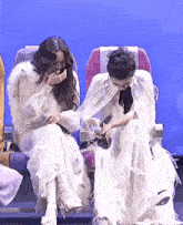 a woman in a white dress is sitting next to another woman in a white dress