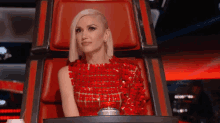 a woman in a red dress is sitting in a red chair on a stage .