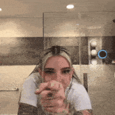 a woman is pointing at the camera in a bathroom while wearing a white shirt .