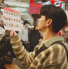 a man in a green and white sweater holds up a menu that says kyungzaeng on it