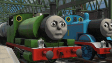 a green train with the number 1 on the front is next to a blue train