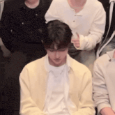 a man in a yellow jacket is sitting in a crowd of people .