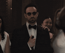 a man in a tuxedo and bow tie is standing in a crowd