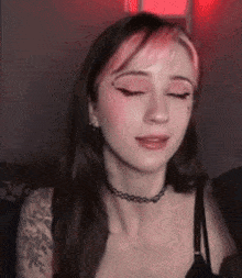 a woman with pink hair and a choker is sitting on a couch .