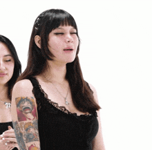 a woman with a tattoo on her arm is standing next to another woman with a tattoo on her arm .