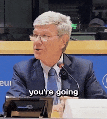a man in a suit and tie is speaking into a microphone and the words you 're going are on the screen
