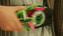 a close up of a person holding a green and pink toy with the letter t on it