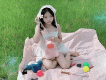 a little girl is sitting on a pink blanket in the grass holding a stuffed animal