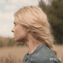 a woman with blonde hair is standing in a field with netflix written in the corner