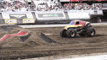 a monster truck is driving on a dirt track with a jcb sign in the background