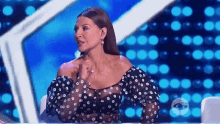 a woman in a black and white polka dot top is sitting at a table in front of a blue background .