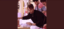 a group of men are standing around a table . one of the men is wearing a black sweater .