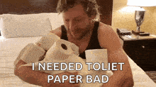 a man is sitting on a bed holding rolls of toilet paper and says i needed toilet paper bad