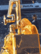 a metlife sign is behind a woman in a gold suit