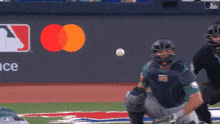 a baseball catcher catches a ball in front of a wall that says mastercard