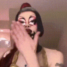 a woman with makeup on her face covering her mouth with her hand