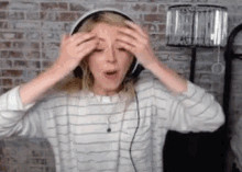 a woman wearing headphones is making a funny face while standing in front of a brick wall .