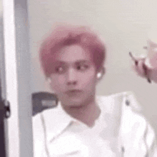 a man with pink hair is wearing a white shirt and ear buds .