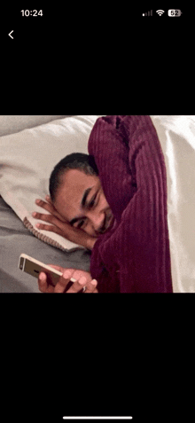 a man laying on a bed looking at a cell phone with the time of 10:24