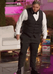 a man in a tuxedo with a crown on his head is standing next to a white chair