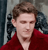 a young man in a red shirt is sitting in a chair with his eyes closed and smiling .