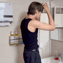 a man in a black tank top is brushing his hair in a bathroom next to a dispenser that says johnson 's