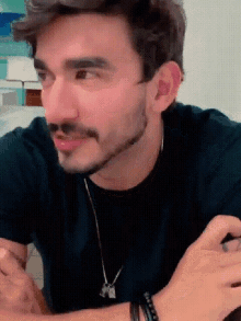a man with a beard wearing a black shirt and a necklace is sitting at a table .