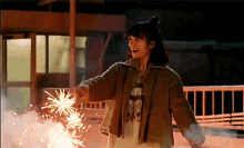 a woman in a brown jacket is holding a firework in her hand