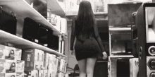 a woman in a black dress is walking through a store filled with televisions and speakers .