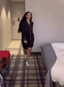 a woman is dancing in a hotel room with a suitcase in the background