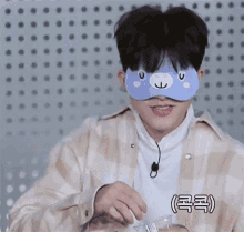 a young man wearing a blue eye mask is holding a glass of water .