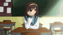 a girl sits at a desk in a classroom with a blackboard behind her