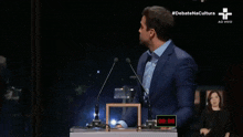 a man in a suit and tie is giving a speech in front of a microphone with the hashtag #debatenacultura above him