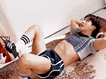 a man in a crop top and shorts is laying on the floor .