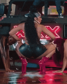 a woman in a green bikini is squatting down in front of a neon sign that says sassy